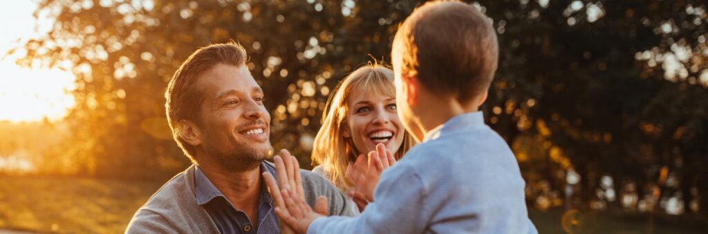 dois pais olhando e sorrindo para seus filhos com um pôr do sol atrás deles