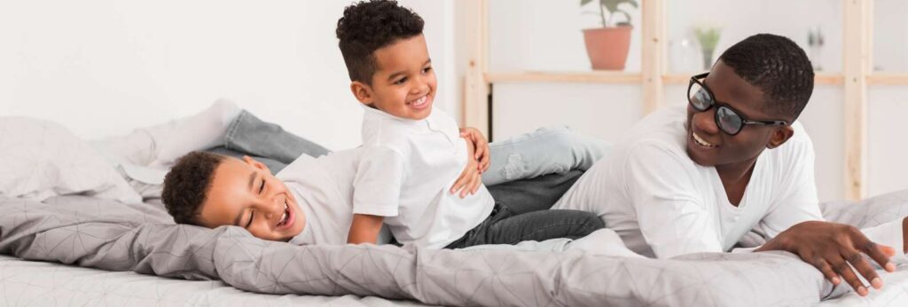 pai brincando com dois filhos na cama dentro de casa