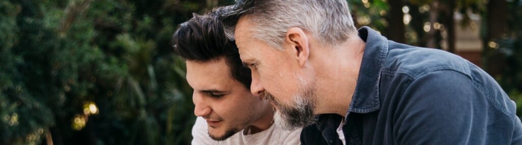 um homem sentado do lado de fora com seu filho olhando para um tablet