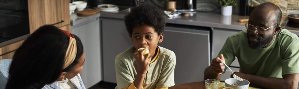 uma criança sentada à mesa de jantar com o pai à direita e a madrasta à esquerda