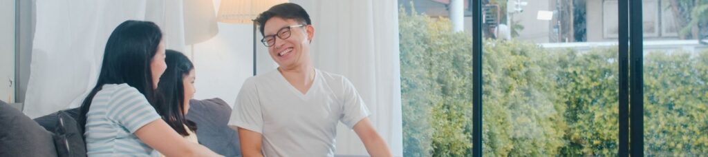 pais e sua filha sentados no sofá com o pai sorrindo para eles