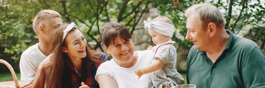 uma avó segurando sua neta sorrindo, com o avô à direita e a filha à esquerda