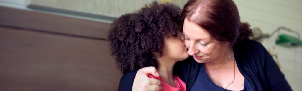 uma garota de ascendência mista beijando o rosto de sua mãe na cama
