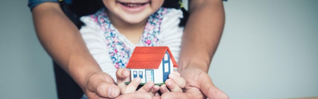 uma mãe e um filho com as mãos juntas segurando uma casa em miniatura