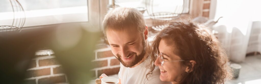 Um casal em casa tomando café e rindo juntos.