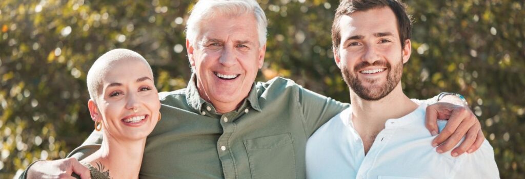 Mulher, seu marido e seu sogro sorrindo para uma foto.